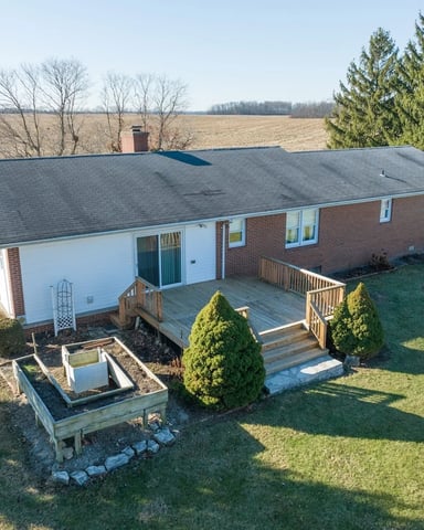 Single-story brick ranch home with deck and garage on rural property overlooking farmland