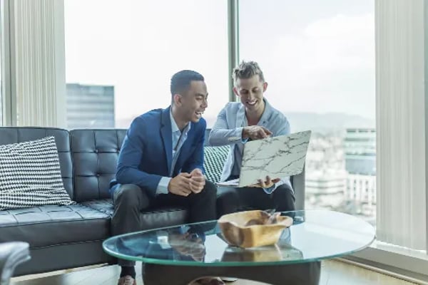 Two professionals reviewing architectural plans on a high-rise office sofa with city skyline view
